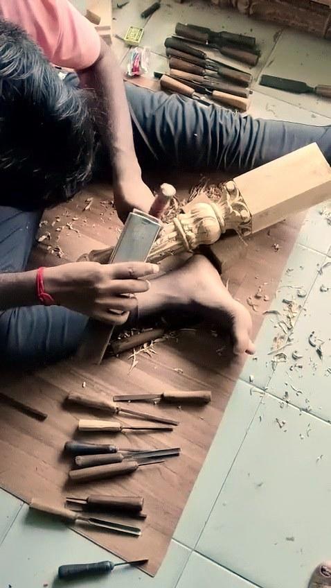 Hands at the chisel, carving a pillar capital on the workshop floor