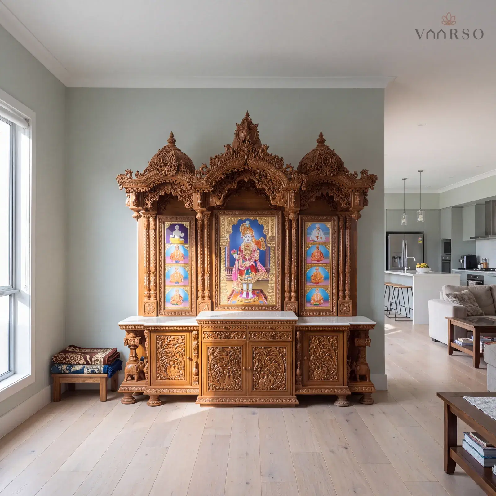 The same mandir in the edge of an open-plan living space, the kitchen away at the far end, wide pale oak boards underfoot and a pair of folded prayer mats on a low stool