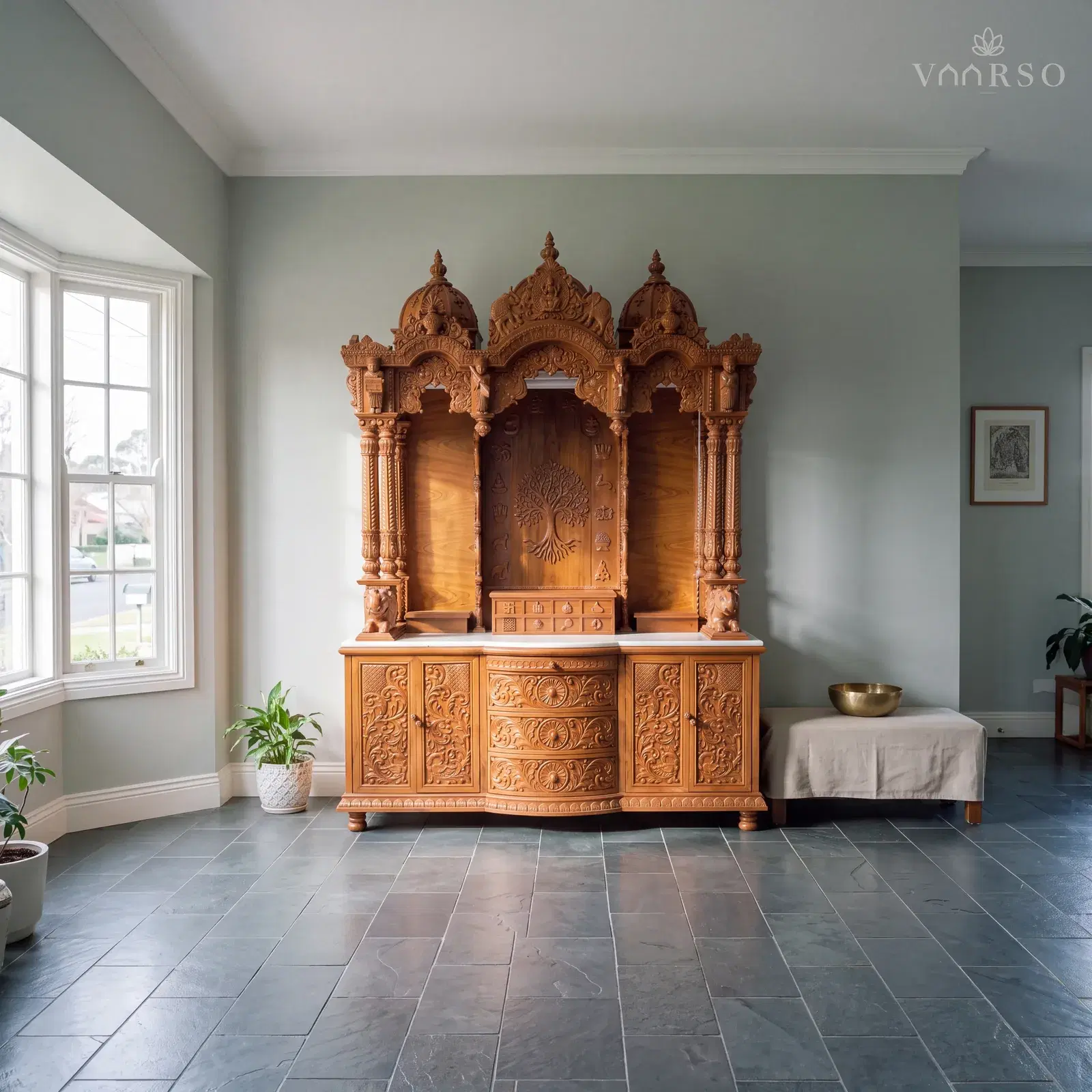 The same mandir in a formal front lounge, a bay window to the street at one side, honed grey slate underfoot and a linen-covered bench carrying a single brass bowl