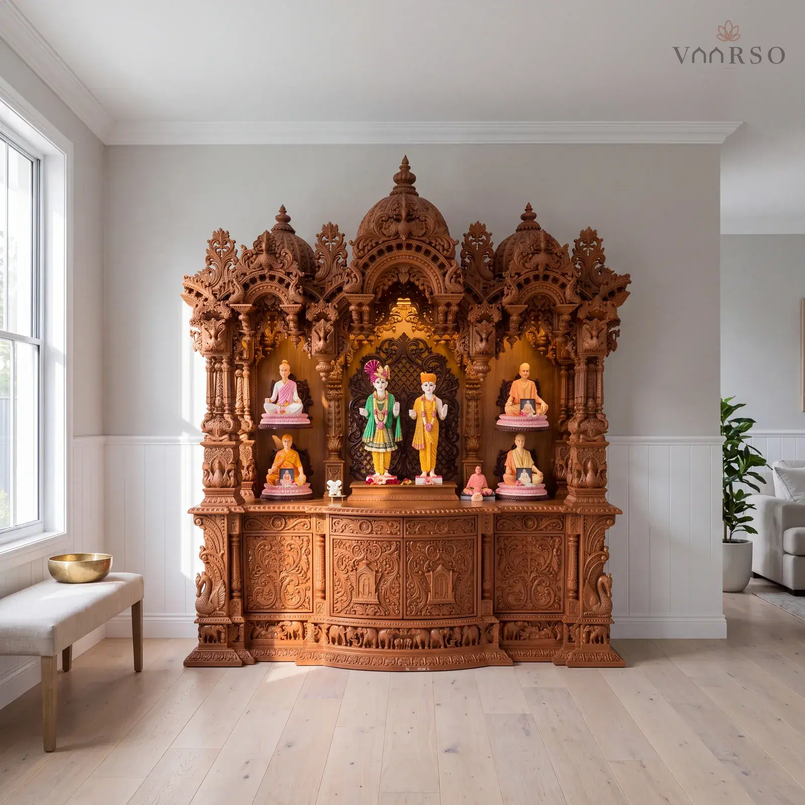 The same mandir in a Hamptons-style living room, shaker panelling below the plaster, wide pale oak boards underfoot and a linen-covered bench carrying a single brass bowl
