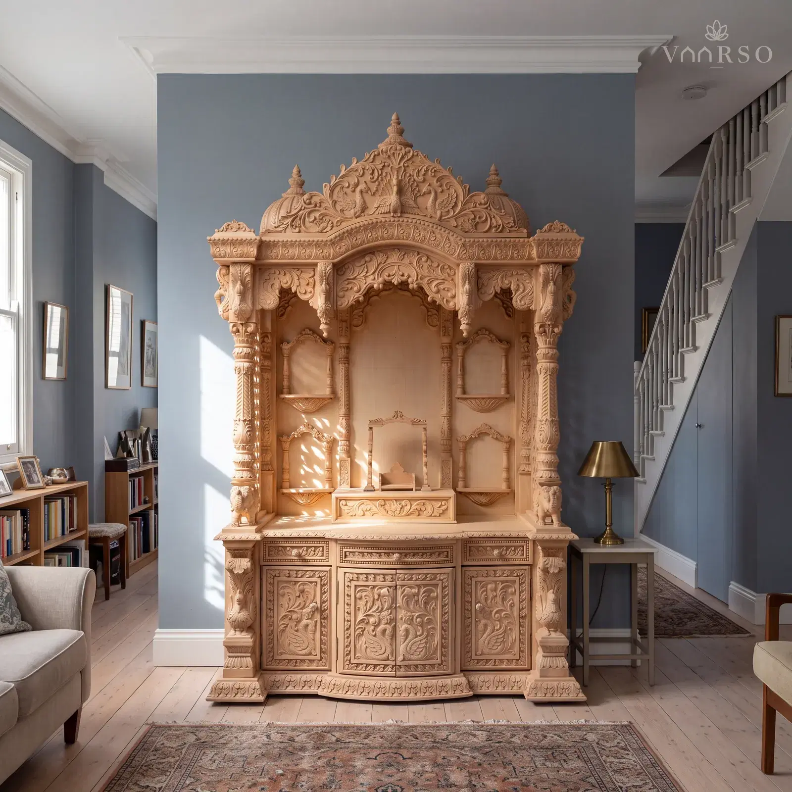 The same mandir in a narrow townhouse living room, the stair rising at the far end, wide pale oak boards underfoot and a worn Persian rug and a brass lamp on a side table