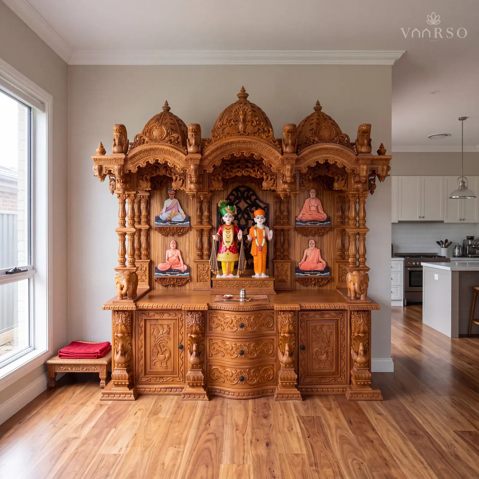 The same mandir in the edge of an open-plan living space, the kitchen away at the far end, spotted gum boards underfoot and a low carved chowki with a folded red cloth on it