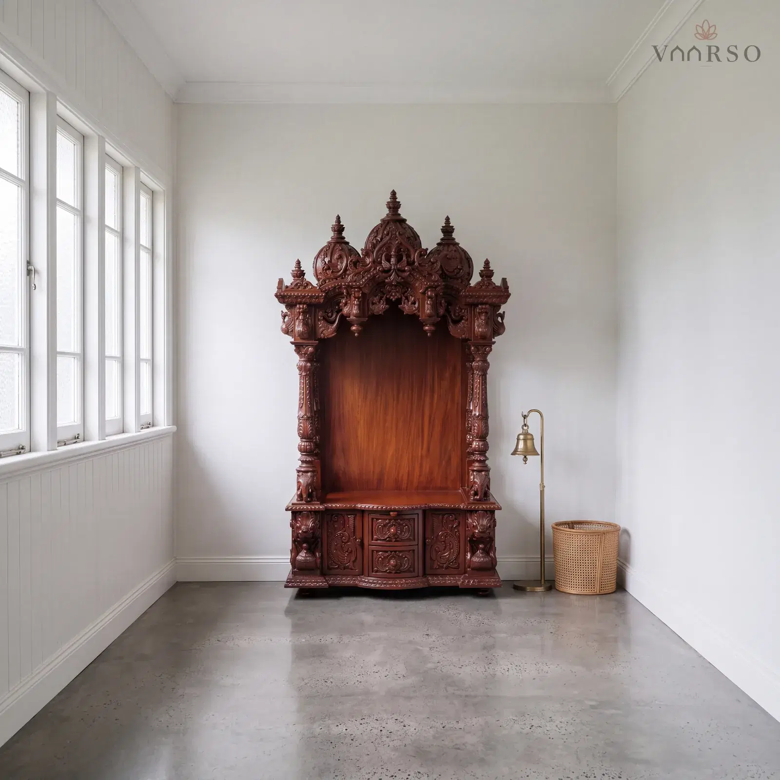The same mandir in an enclosed verandah room, casement windows along one side, polished concrete underfoot and a brass bell on a floor stand and a cane basket beside it