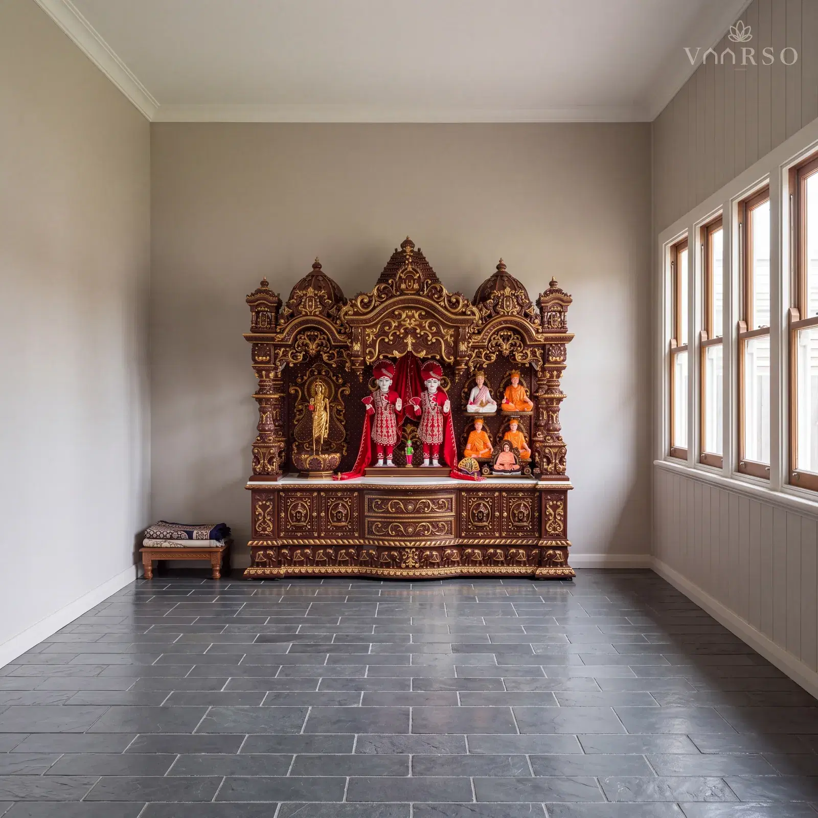 The same mandir in an enclosed verandah room, casement windows along one side, honed grey slate underfoot and a pair of folded prayer mats on a low stool