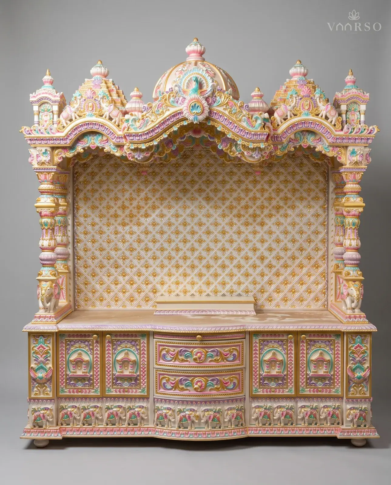 A wide mandir in cream polish picked out in pastel colours and gold, shikhars and a peacock dome across the crest, a gold-patterned backboard behind the empty shrine, elephants at the columns, and carved drawers over a plinth of elephants