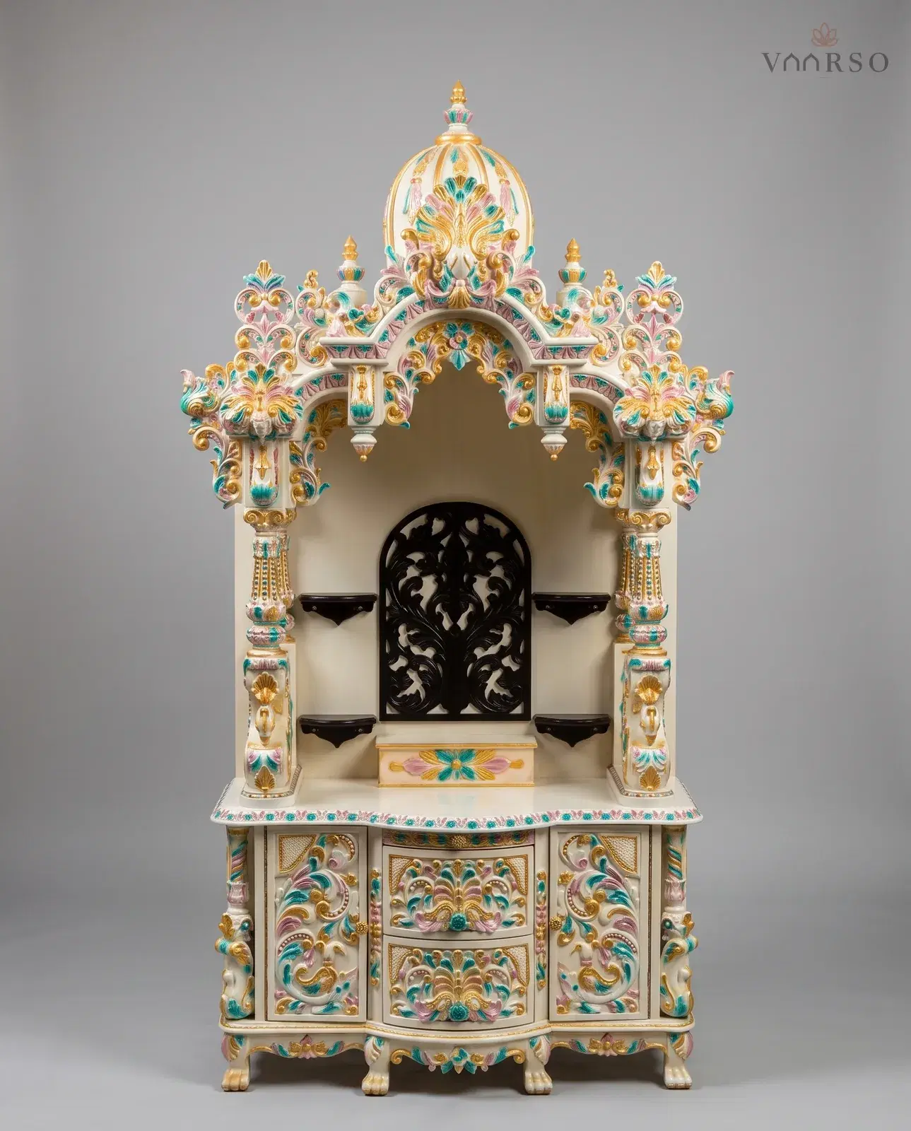 A tall mandir in cream polish picked out in pink, turquoise and gold, a ribbed dome over a scalloped arch, a black pierced panel between four black shelves, and carved drawers between two cupboards on claw feet