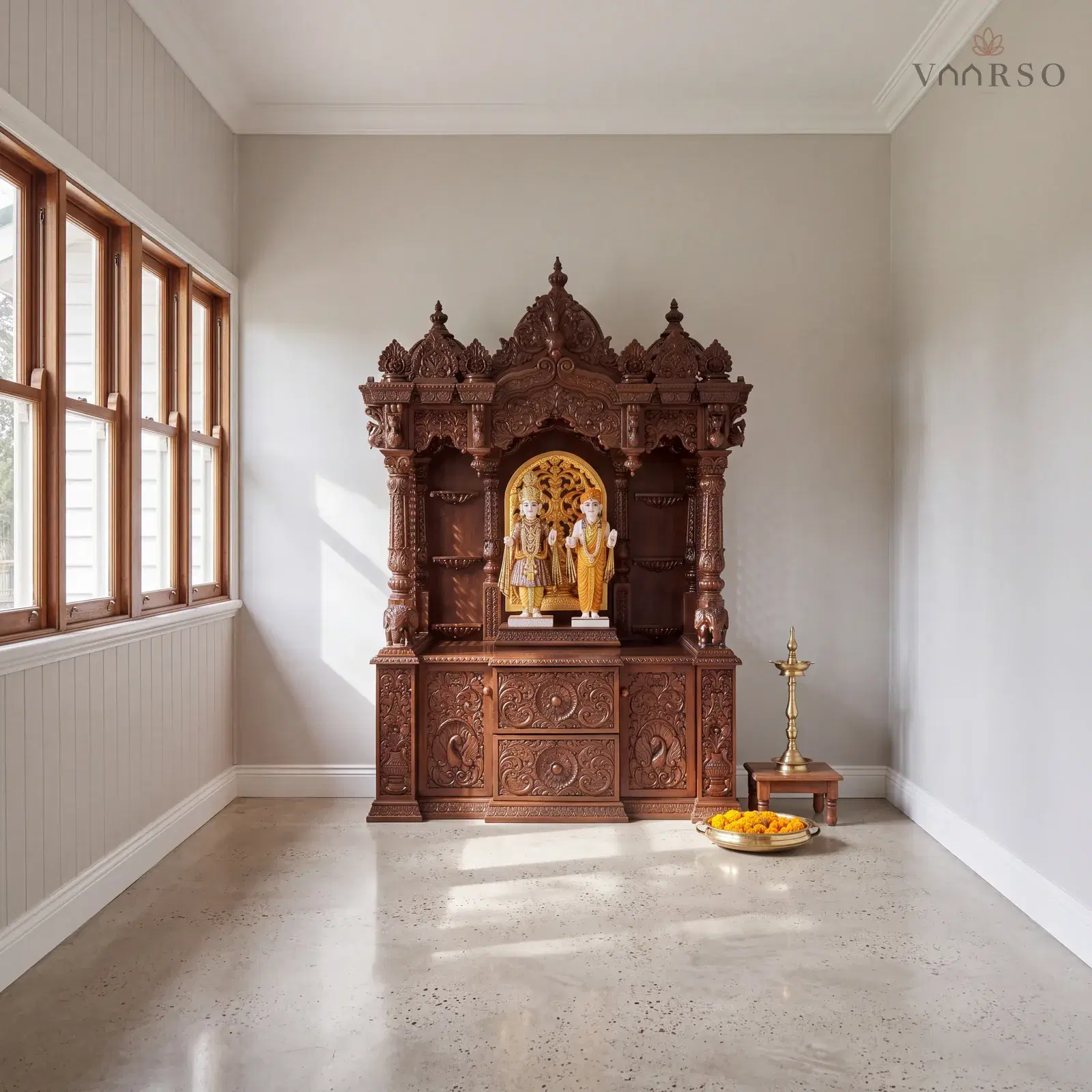 The same mandir in an enclosed verandah room, casement windows along one side, polished concrete underfoot and a brass oil lamp on a timber stool and a thali of marigolds on the floor