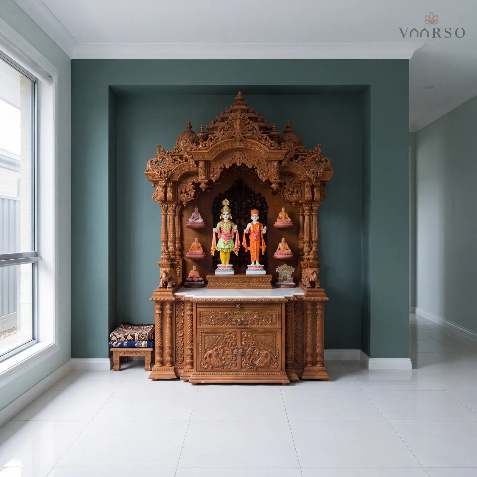 The same mandir in a wide hallway nook, set into the recess, white porcelain tile underfoot and a pair of folded prayer mats on a low stool