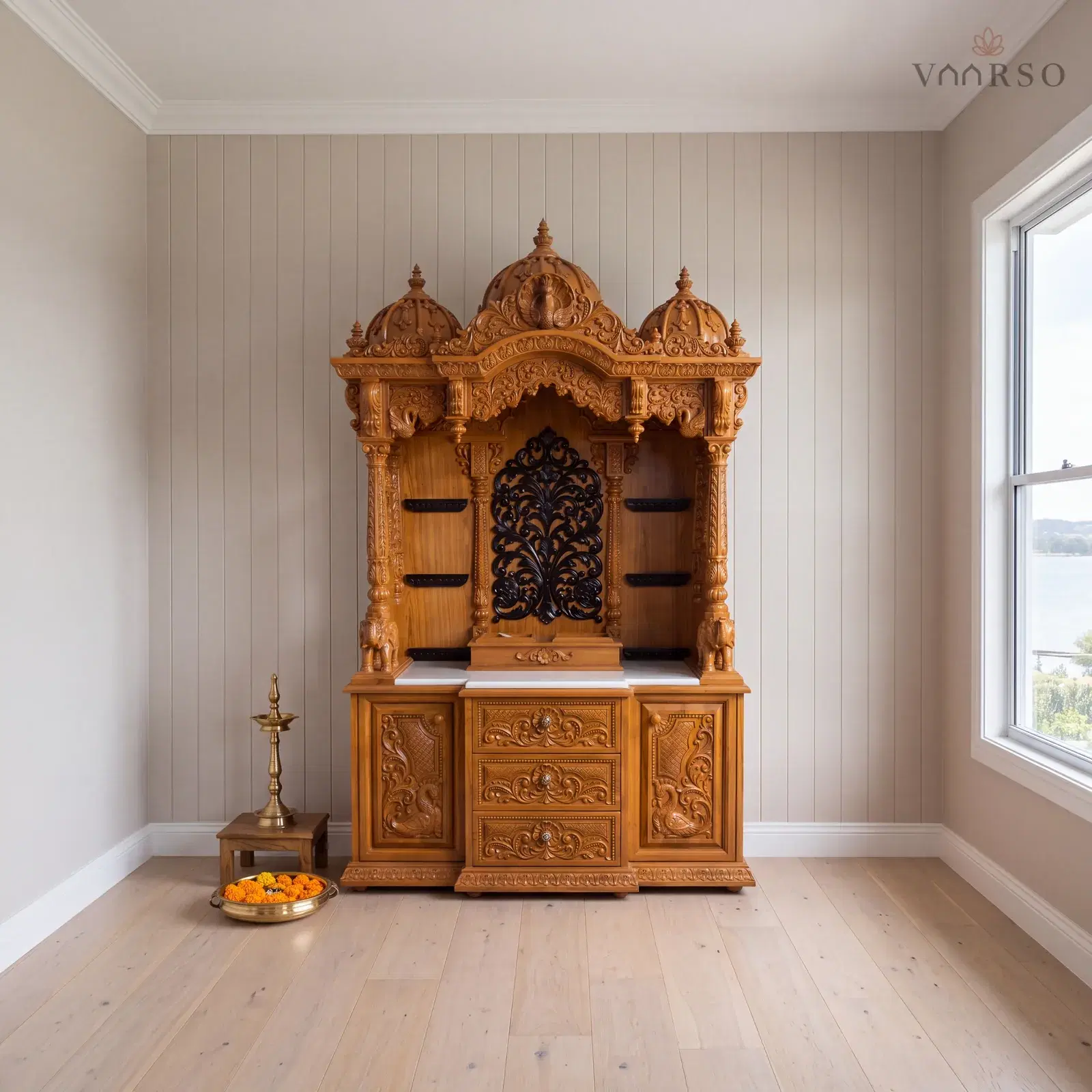 The same mandir in a coastal living room, VJ board panelling behind it, wide pale oak boards underfoot and a brass oil lamp on a timber stool and a thali of marigolds on the floor