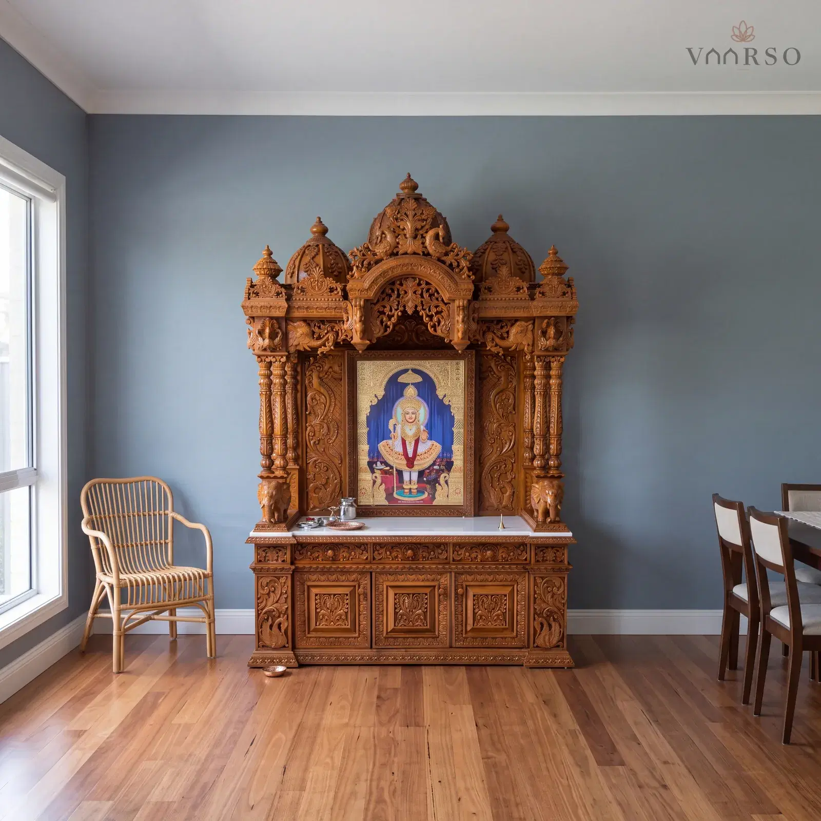 The same mandir in the dining end of an open-plan room, the table well away at the far side, blackbutt boards underfoot and a rattan armchair turned toward it