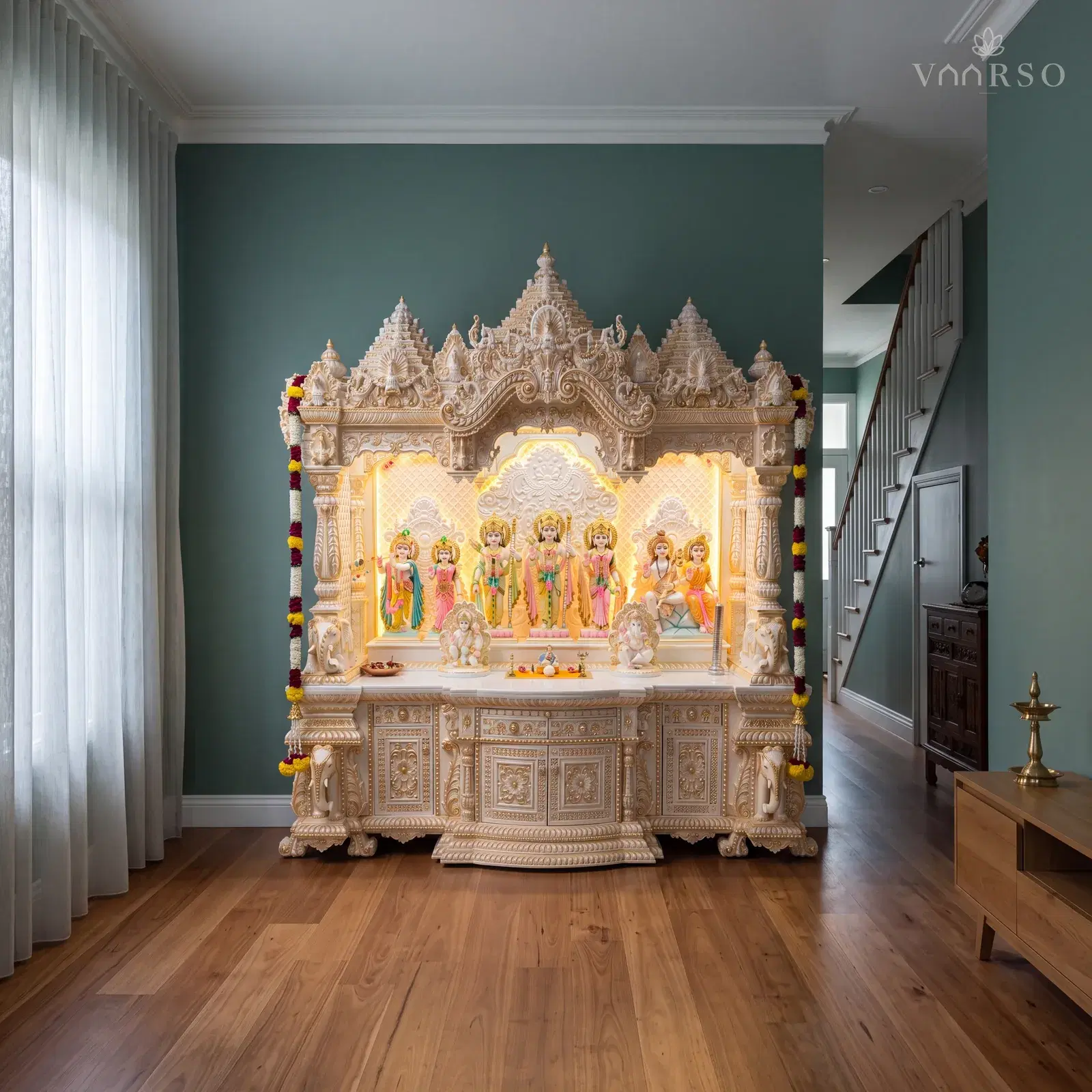 The same mandir in a narrow townhouse living room, the stair rising at the far end, blackbutt boards underfoot and a low timber console carrying a single brass diya